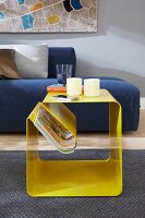 Yellow side table with magazines and book in front of blue sofa