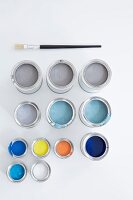 Blue, grey, black, white and yellow paint in colour pots on white background