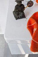 Close-up of white vanity sink with orange towel and incense holder statue
