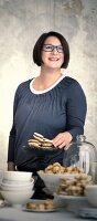 Happy woman wearing gray top with long sleeves standing beside cookies