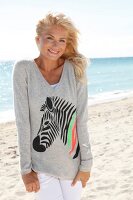 Portrait of pretty woman wearing gray top standing on beach, smiling