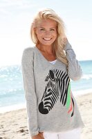 Portrait of pretty woman wearing gray top standing on beach, smiling