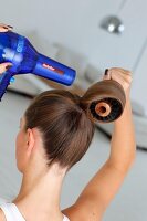 Rear view of woman holding round hair brush and blow drying her hair