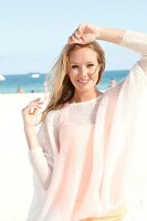 Blonde woman in a white sweater on the beach, smiling at camera