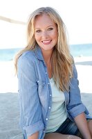 Blonde woman in a denim shirt smiles at the camera on the beach