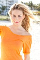 Blonde woman with long hair wearing an orange t-shirt on the beach