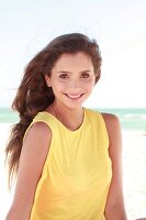 Frau mit langen dunklen Haaren im gelben Shirt am Strand