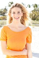 Blonde woman with long hair wearing an orange t-shirt on the beach