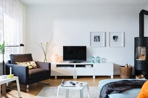 A black armchair in front of a television unit with a Scandinavian wood stove in a living room