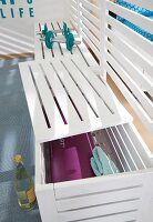 A white painted bench made from wooden slats used as a room divider and as storage for sports equipment