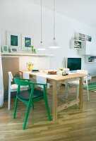A dining area in an open plan living room, a simple solid wood table with white chairs and one green chair
