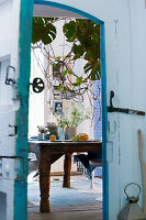 View through open door of wooden table with crockery and plant decoration in dining room