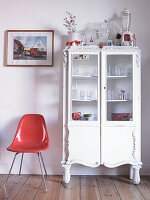 White vintage display cabinet next to red chair