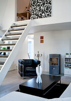 Living room with black leather armchair, stove and staircase