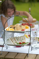 Etagere mit Sandwiches, Scones und Obst im Garten