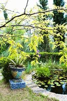Planter decorated with colourful irregular mosaic next to pond in Mediterranean garden