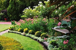 Shady seating area with garden bench in magnificently flowering garden with manicured lawns