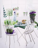 Gartentischgarnitur aus weißem Metall - Blumentopf mit Übertopf aus Metallgeflecht neben Bechern auf Tischläufer