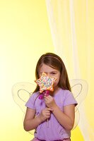 Mädchen mit Engelsflügeln hält einen sternförmigen Cake Pop mit bunten Streuseln in der Hand