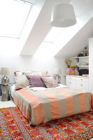 Doppelbett in weißem Dachgeschosszimmer mit orangefarbenen Akzenten