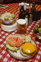 A cheeseburger, beer and pickled gherkins on a checked tablecloth