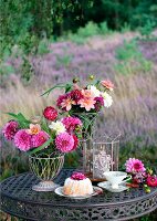 Gedeckter Gartentisch mit Napfkuchen, Teetasse, Sommerblumen und Windlicht