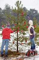 Paar schmückt einen Christbaum im Wald