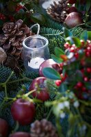 Weihnachtsgesteck aus Tannenzweigen, Scheinbeeren, Lorbeer, Äpfeln, Misteln und Pinienzapfen mit Windlicht