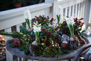 Weihnachtsgesteck aus Tannenzweigen, Scheinbeeren, Lorbeer, Äpfeln, Misteln, Hyazinthen und Pinienzapfen mit Windlicht auf der Terrasse