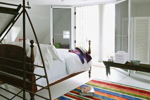 Moderner, offener Schlafbereich mit antikem Bett gegenüber offener Terrassen-Flügeltür und teilweise sichtbarer Teppichläufer mit bunten Streifen