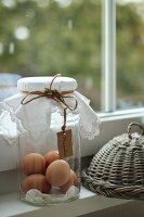 Brown eggs in a storage jar and a wicker cover on the windowsill