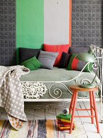 Tagesbett mit nostalgischem Bettgestell und bunten, selbstgenähten Zierkissen vor Wand mit breitem Streifenmuster