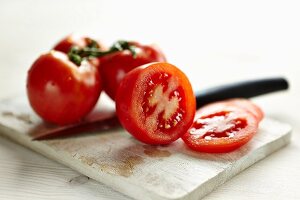 Aufgeschnittene Tomate und ganze Toamten auf Brett mit Messer