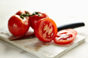 Sliced tomatoes and whole tomatoes on a board with a knife