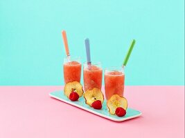 Three glasses of pink lady apple frappe, decorated with a slice of apple and a raspberry