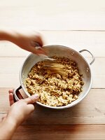 Oat and butter mixture in a metal bowl being stirred by hand