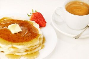 Pancakes mit Butter, Ahornsirup, Erdbeere und einer Tasse Kaffee