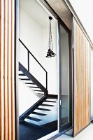 Bundle of pendant lamps above purist steel staircase seen through angled, glass sliding door and vertical slatted screen