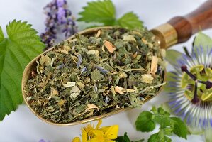 A mix for herbal tea, made with lemon balm, passion flowers, St. John's wort, hops, lavender and orange flowers on a brass scoop