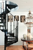 Black, metal, vintage spiral staircase next to various ceramic vases on table below chandelier