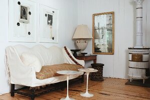 White plastic side tables in front of antique bench with ecru loose cover and white, vintage wood-burning stove