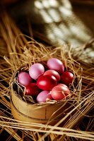 Pink and red Easter eggs in straw in a woodchip basket