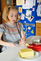 Mädchen schneidet Butterstück ab in der Küche