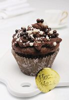 A chocolate cupcake decorated with chocolate and sugar pearls