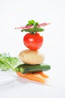 A stack of vegetables consisting of carrots, courgettes, a potato, a tomato, a pea pod and a borlotti bean