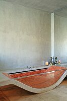 Badewanne aus gebogener Betonplatte und Seitenwand aus Glas, innenseitig rote Mosaikfliesen in minimalistischem Bad