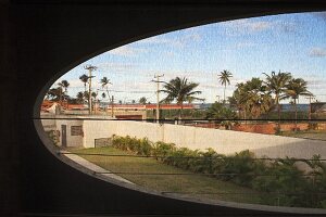 Ovaler Ausschnitt in Betonfassade mit Ausblick auf Palmen in städtischer Umgebung