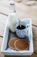 Kaffee, Sirupwaffeln und Milchflasche auf Tablett