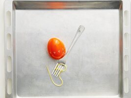 An egg timer and a fork with a strand of spaghetti on a baking tray