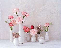 Verschiedene rosafarbene Blüten in weissen Vasen